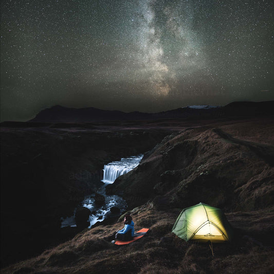 Travel outdoor Iceland photography print featuring Milky Way and a lonely hiker sitting by a tent and a waterfall